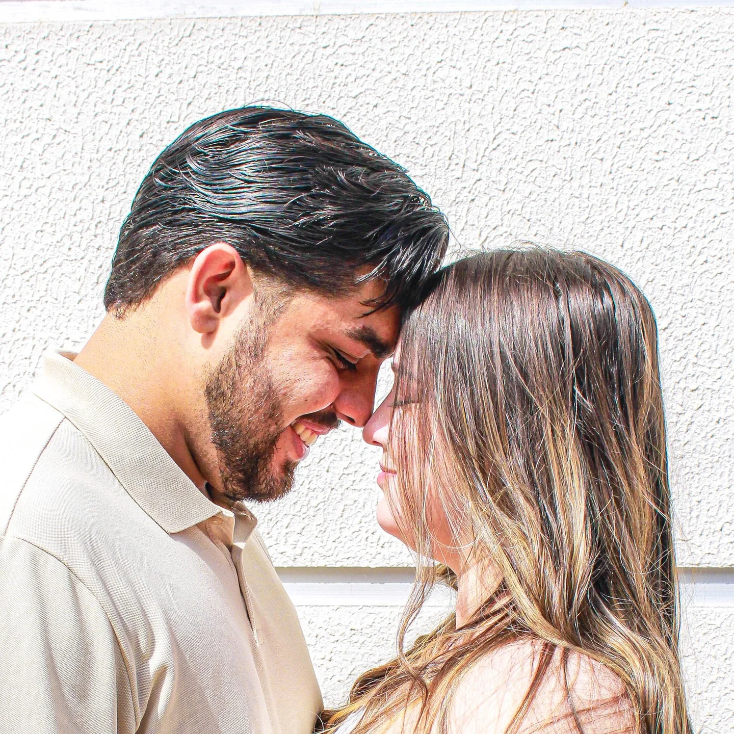 Casal com as testas encostadas diante de uma parede clara.