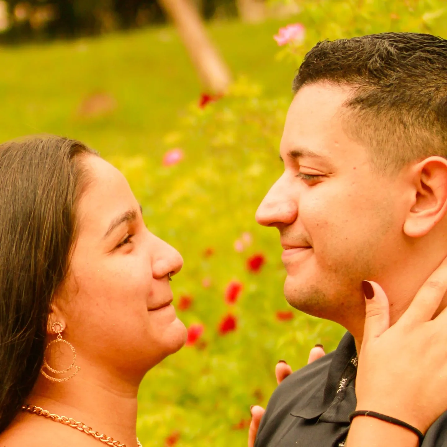Casal se olha de perto diante de um jardim.