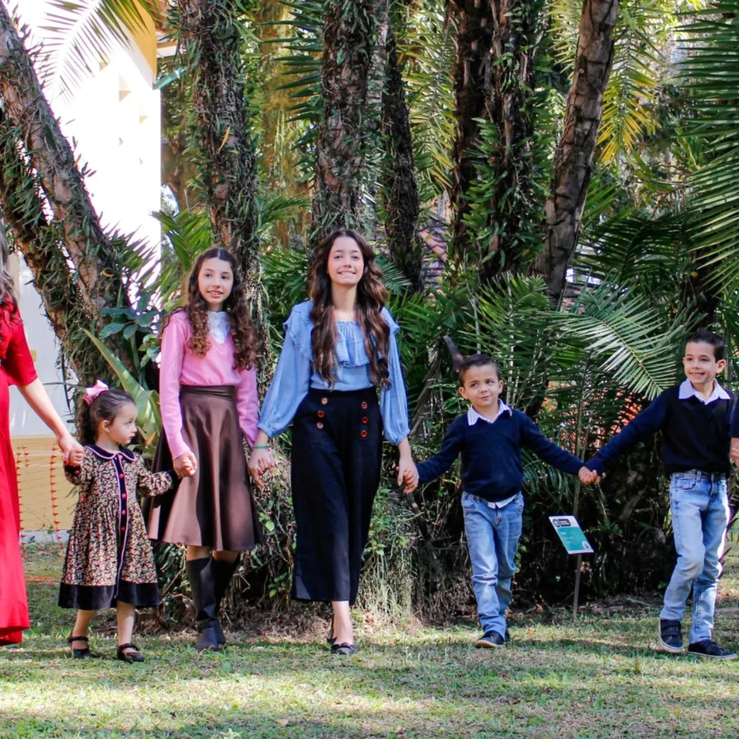Crianças de mãos dadas posam entre árvores em um jardim.