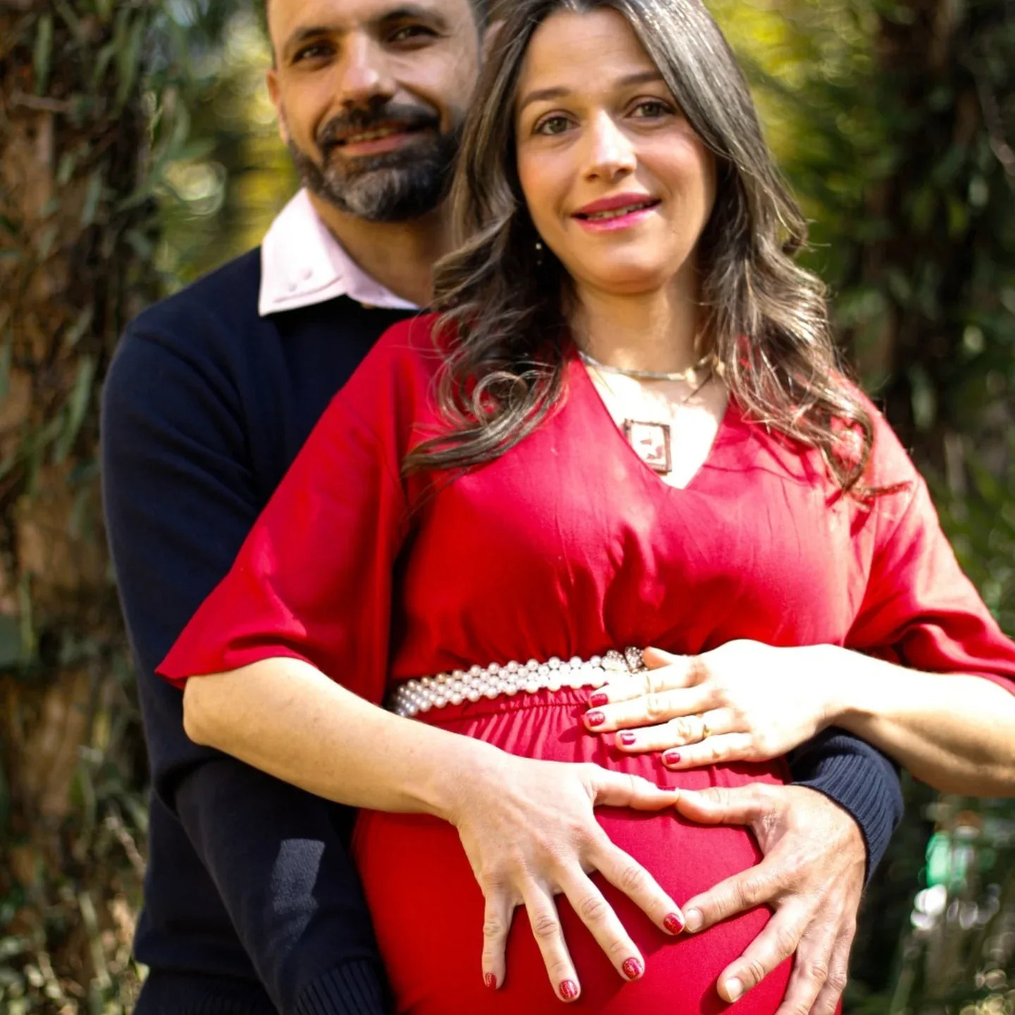 Mulher de vestido vermelho e homem de blusa azul posam juntos em um jardim.
